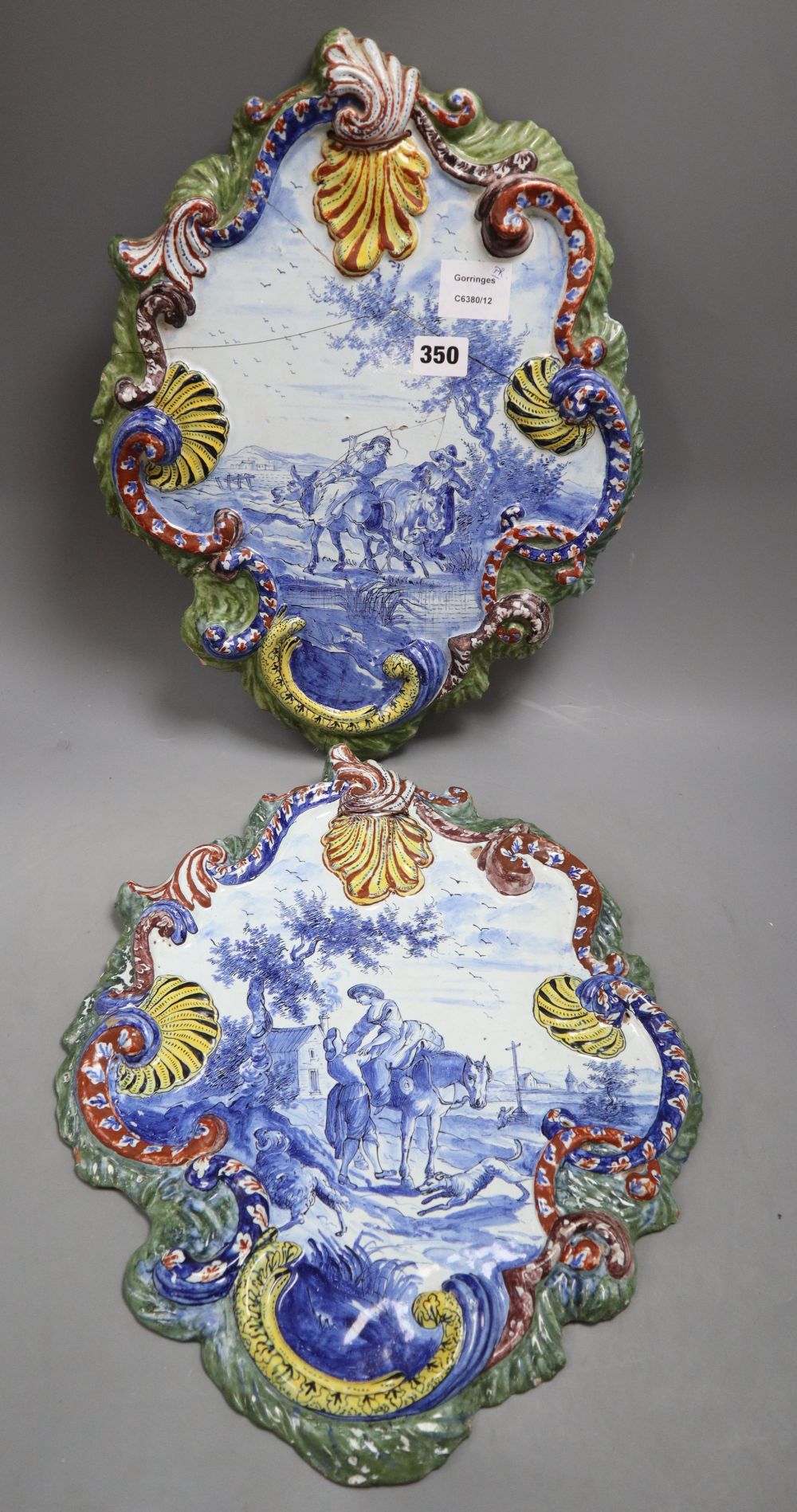 A pair of tinglaze blue and white cartouche shaped wall plaques, 19th century, each with polychrome painted rocaille borders, 32 x 42cm